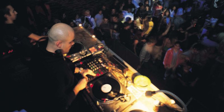 Un discjòquei posa música en l’interior d’una discoteca, mentre els joves ballen.