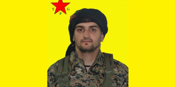 Samuel Prada vestit de milicià i davant la bandera de les milícies kurdes YPG.