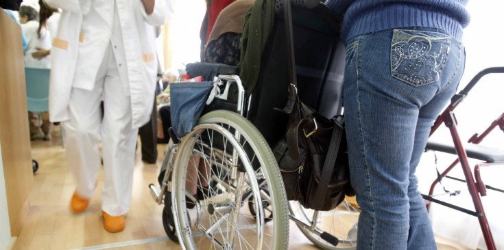 Una persona porta al seu familiar amb cadira de rodes en un centre assistencial del país.