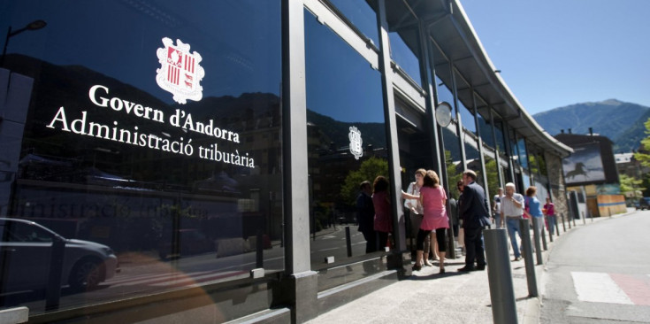 Entrada de l’edifici de l’Administració tributària del Govern d’Andorra, amb alguns ciutadans en la porta.